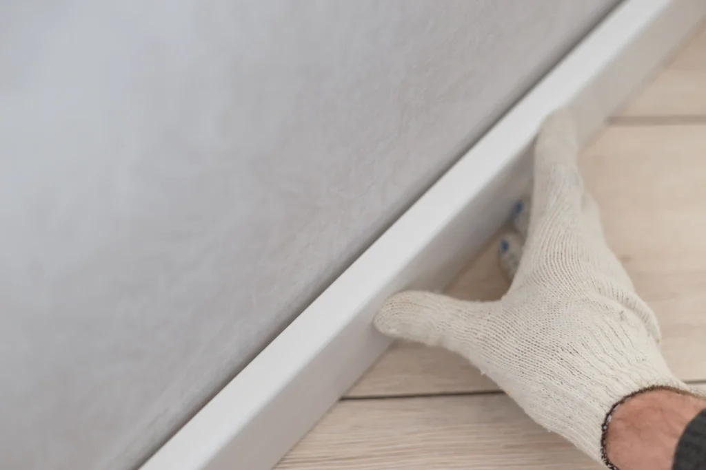Une mai gantée qui met en place une plinthe contre un mur