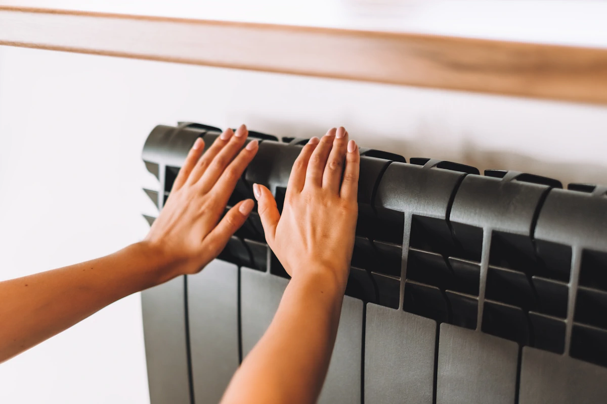 Une personne qui tient un radiateur électrique noir contre le mur