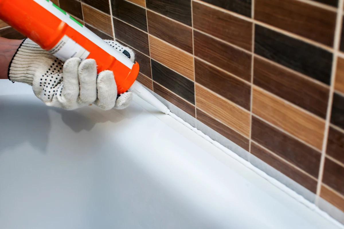 Une personne qui refait les  joints autour de la baignoire