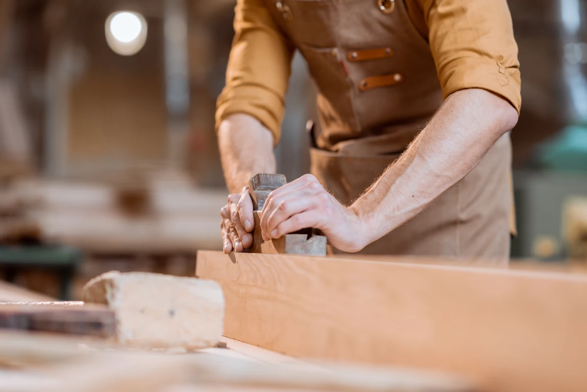 Un homme qui rabote manuellement un portail en bois