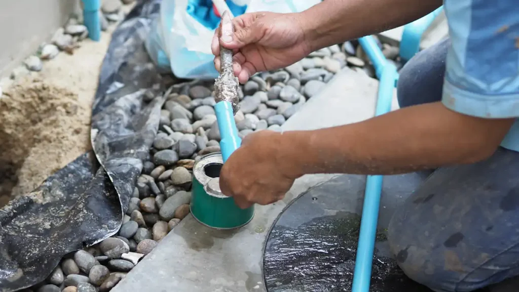 Une personne qui répare un tuyau arrosage percé avec colle étanche
